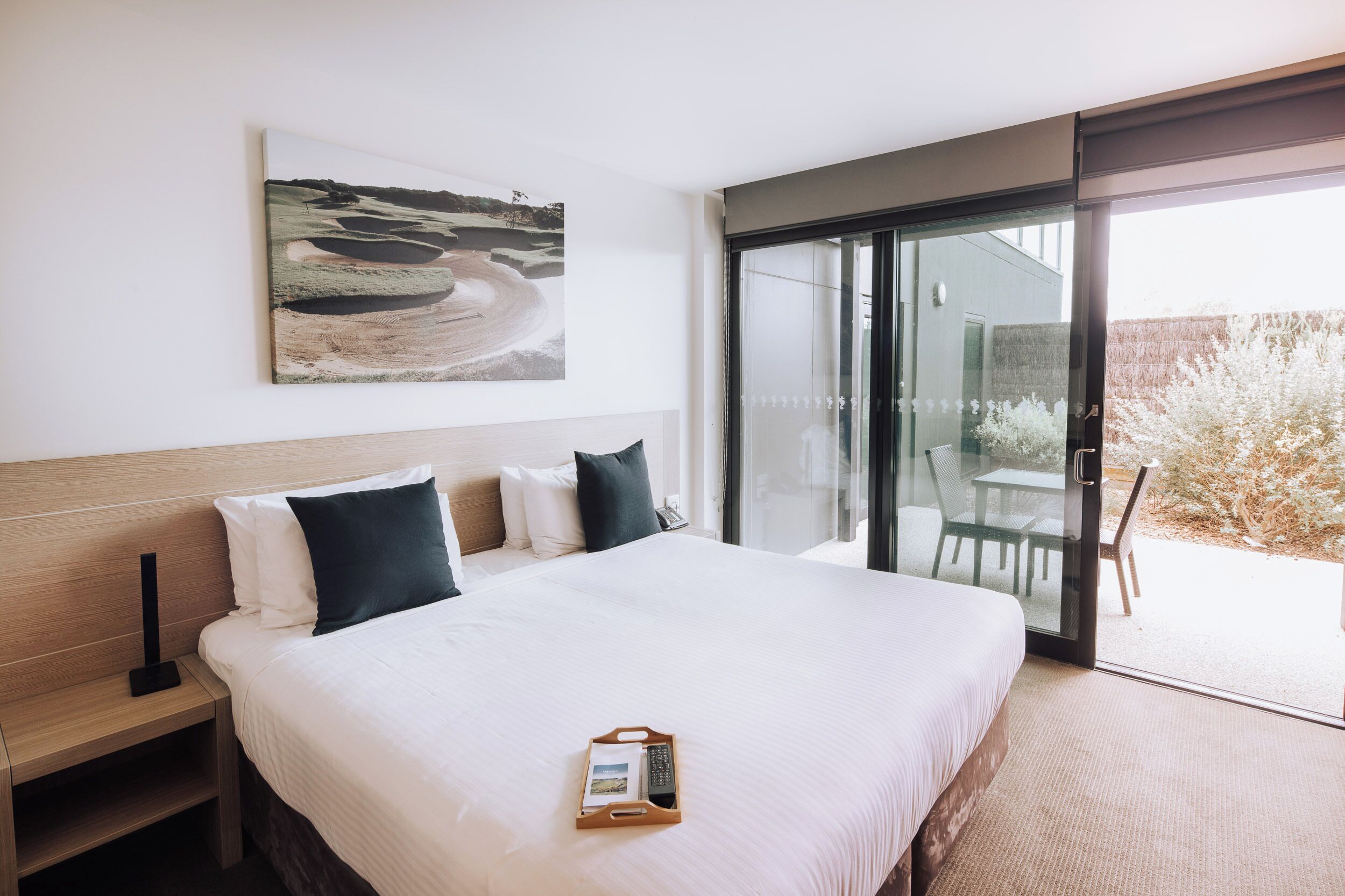 Ein modernes Hotelzimmer mit einem großen Bett, einem Nachttisch, einer Fernbedienung und einer Glastür zu einem Außenbereich.