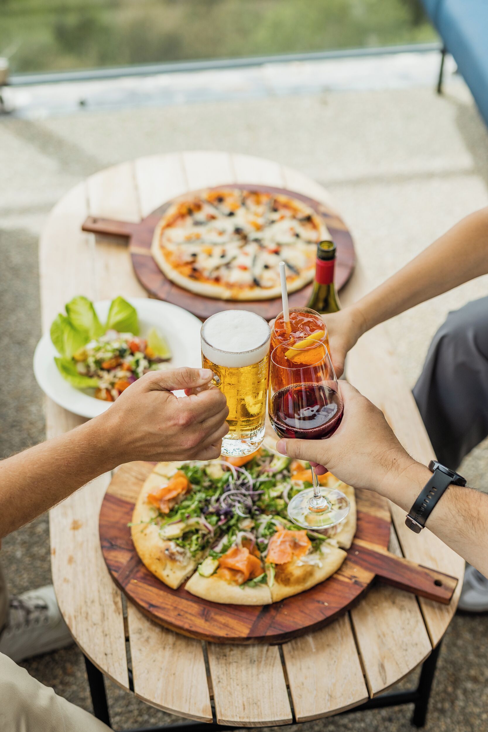 A wooden table with two pizzas and a salad.