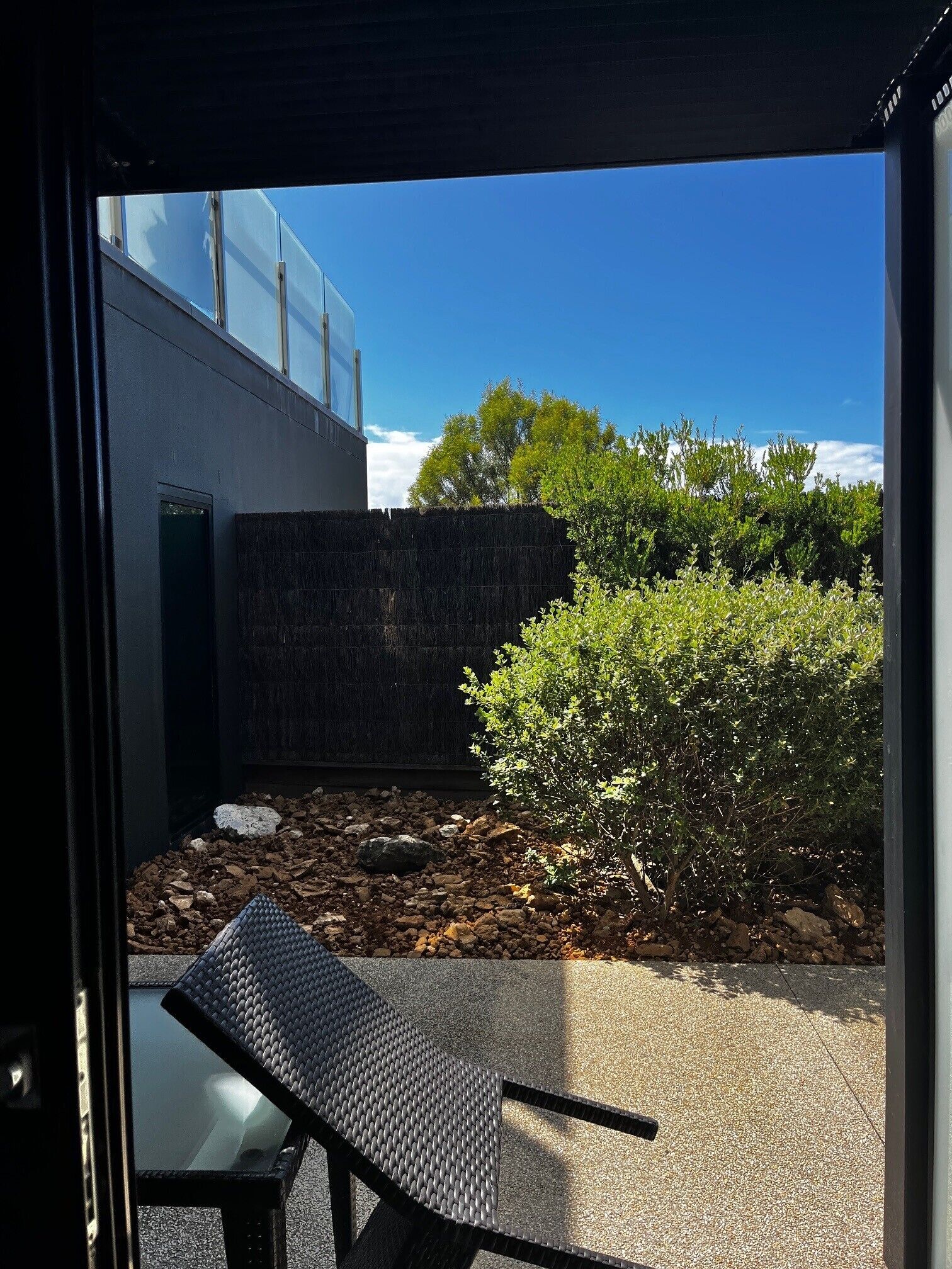 Un área de estar moderna al aire libre con una mesa y sillas de metal, un muro de piedra y vistas a un edificio con ventanas amplias.