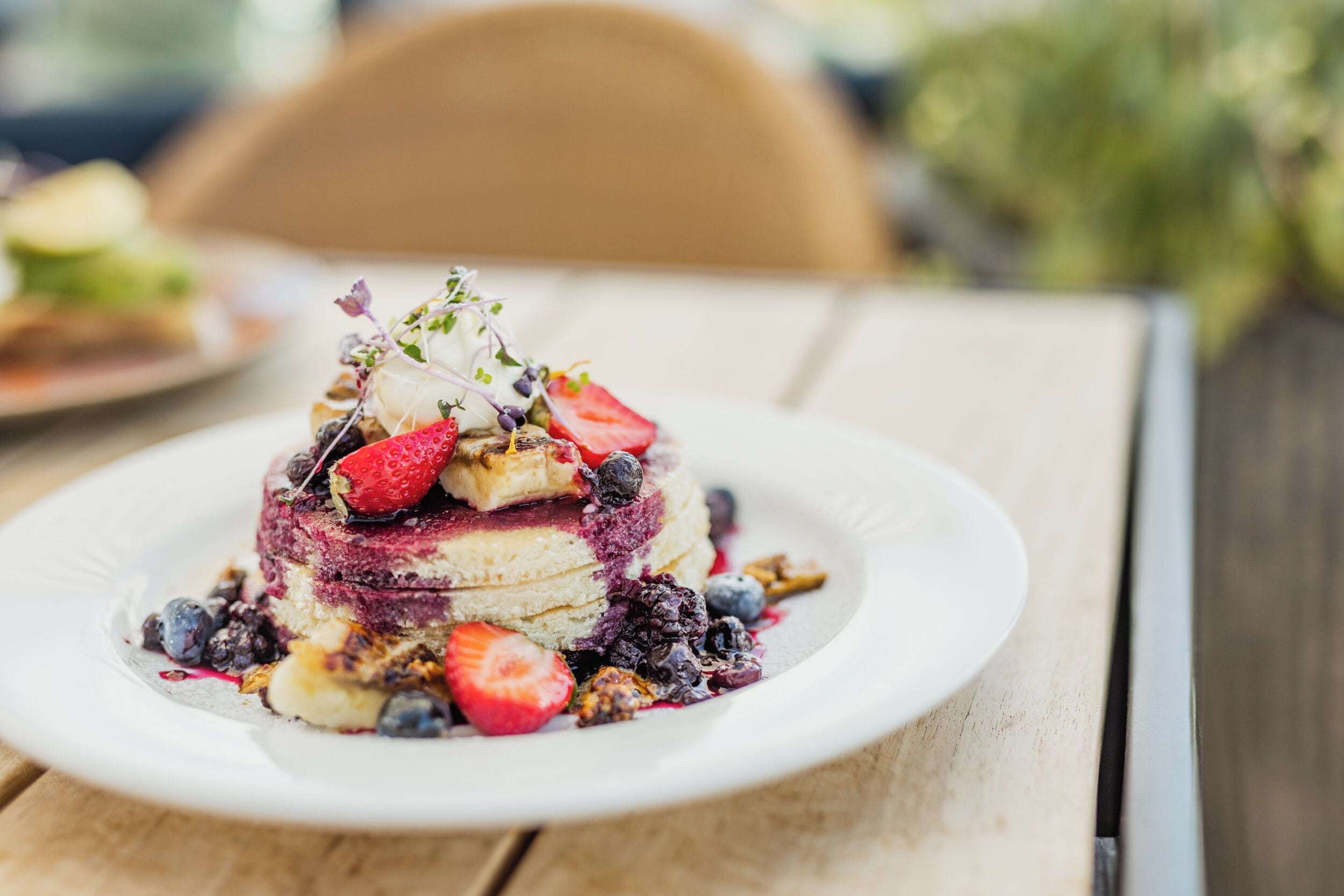 Ein Stapel Pfannkuchen mit Beeren und einem kleinen Kräuterzweig auf einem weißen Teller.