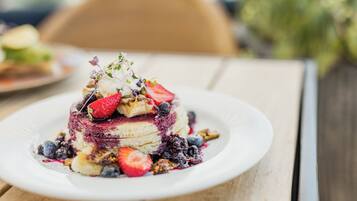 Ein Stapel Pfannkuchen mit Beeren und einem kleinen Kräuterzweig auf einem weißen Teller.