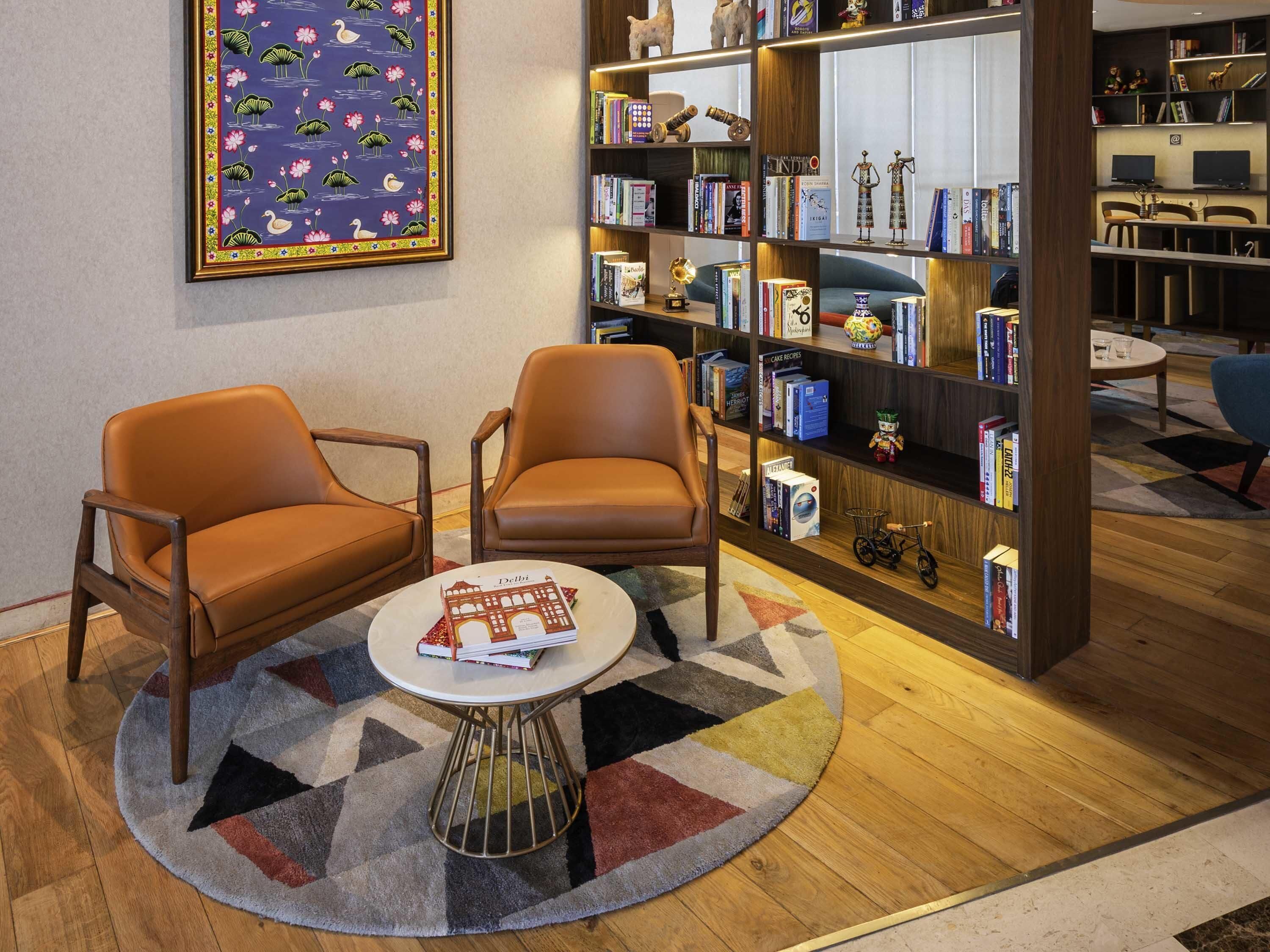 Una habitación con dos sillones de cuero, una mesa de centro, una estantería y un cuadro enmarcado en la pared.