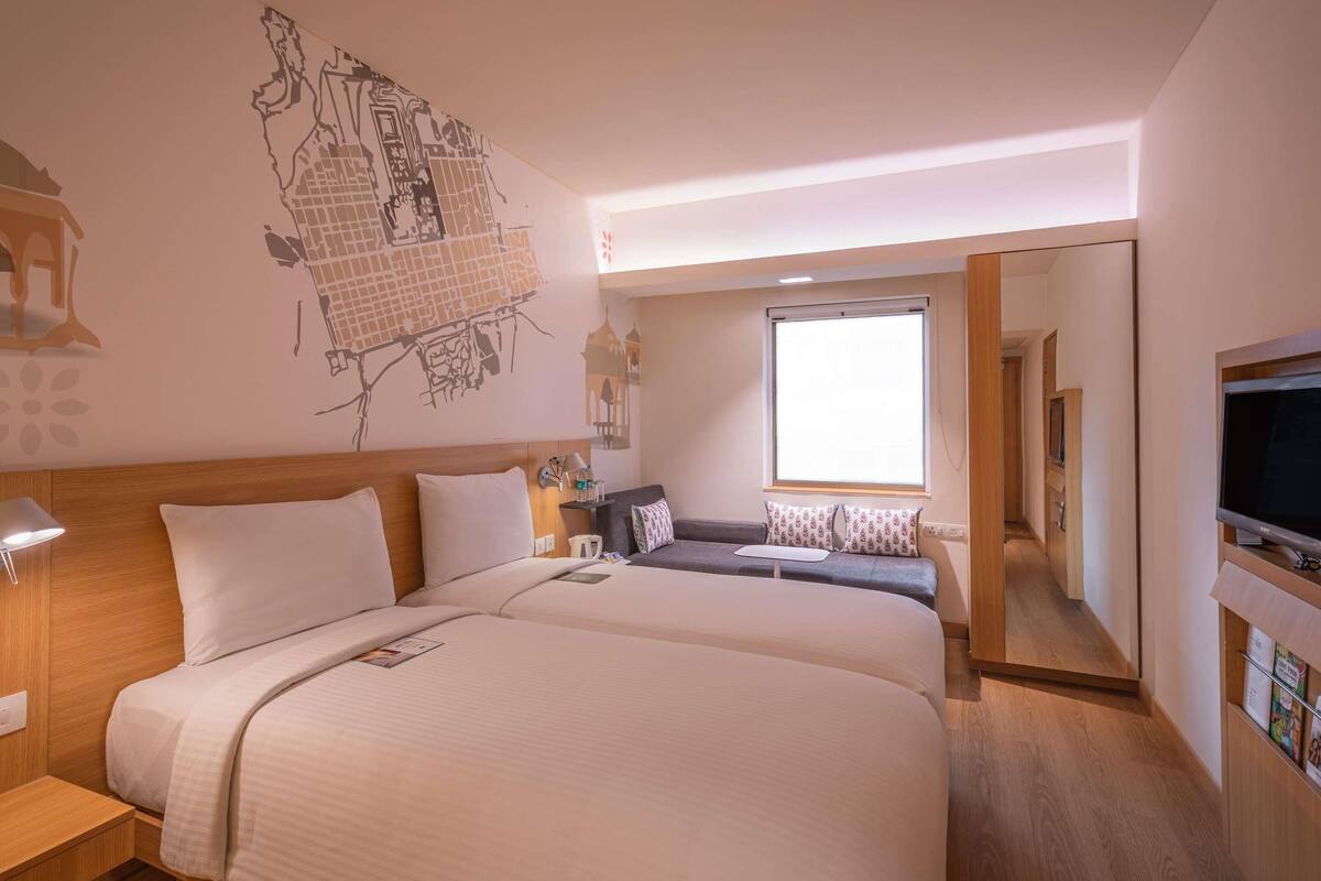 Habitación de hotel con dos camas, televisión, ventana y un mural con un mapa en la pared.