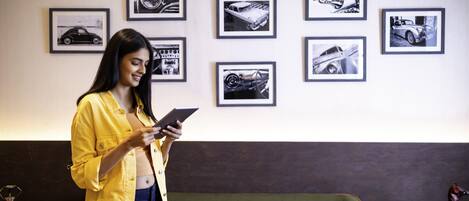 Una persona de pie en una habitación con un sofá verde, una mesa con un adorno y varias fotografías enmarcadas de coches en la pared.