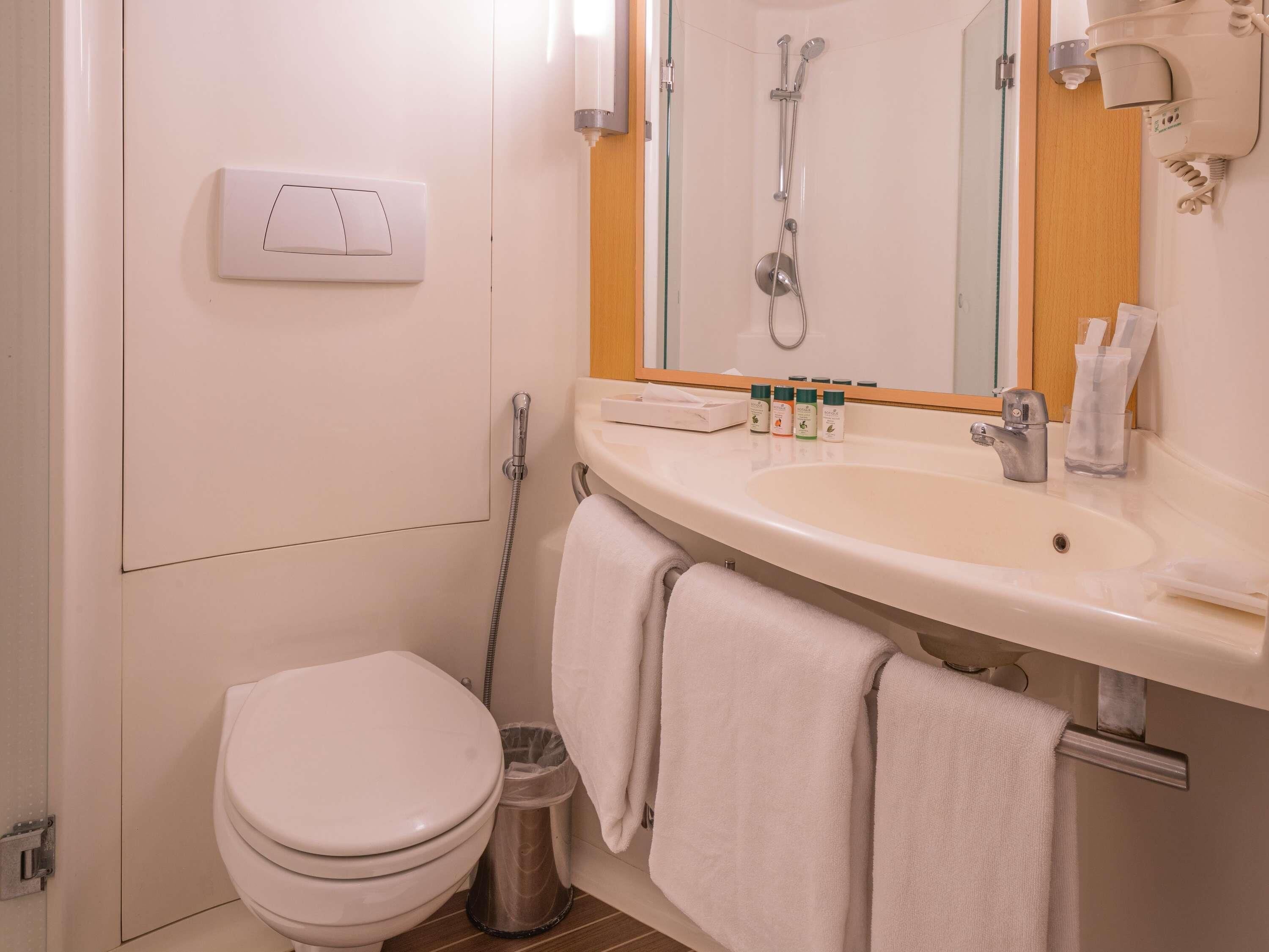 A bathroom with a toilet, sink, shower, and a towel rack.