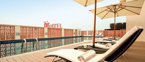 A poolside area with lounge chairs, umbrellas, and a pool.