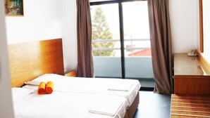 Habitación de hotel con cama, cabecera de madera, escritorio y vistas al exterior a través de una ventana con cortinas.