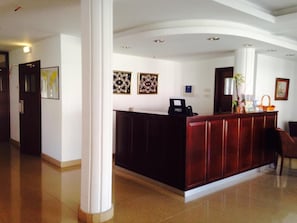 A reception area with a wooden reception desk, a white pillar, and framed artwork on the wall. - Rebioz Hotel (Larnaca)