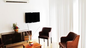 Una sala de estar moderna con un televisor de pantalla plana, un mueble de madera, dos sillones de cuero y una mesita con un jarrón decorativo.