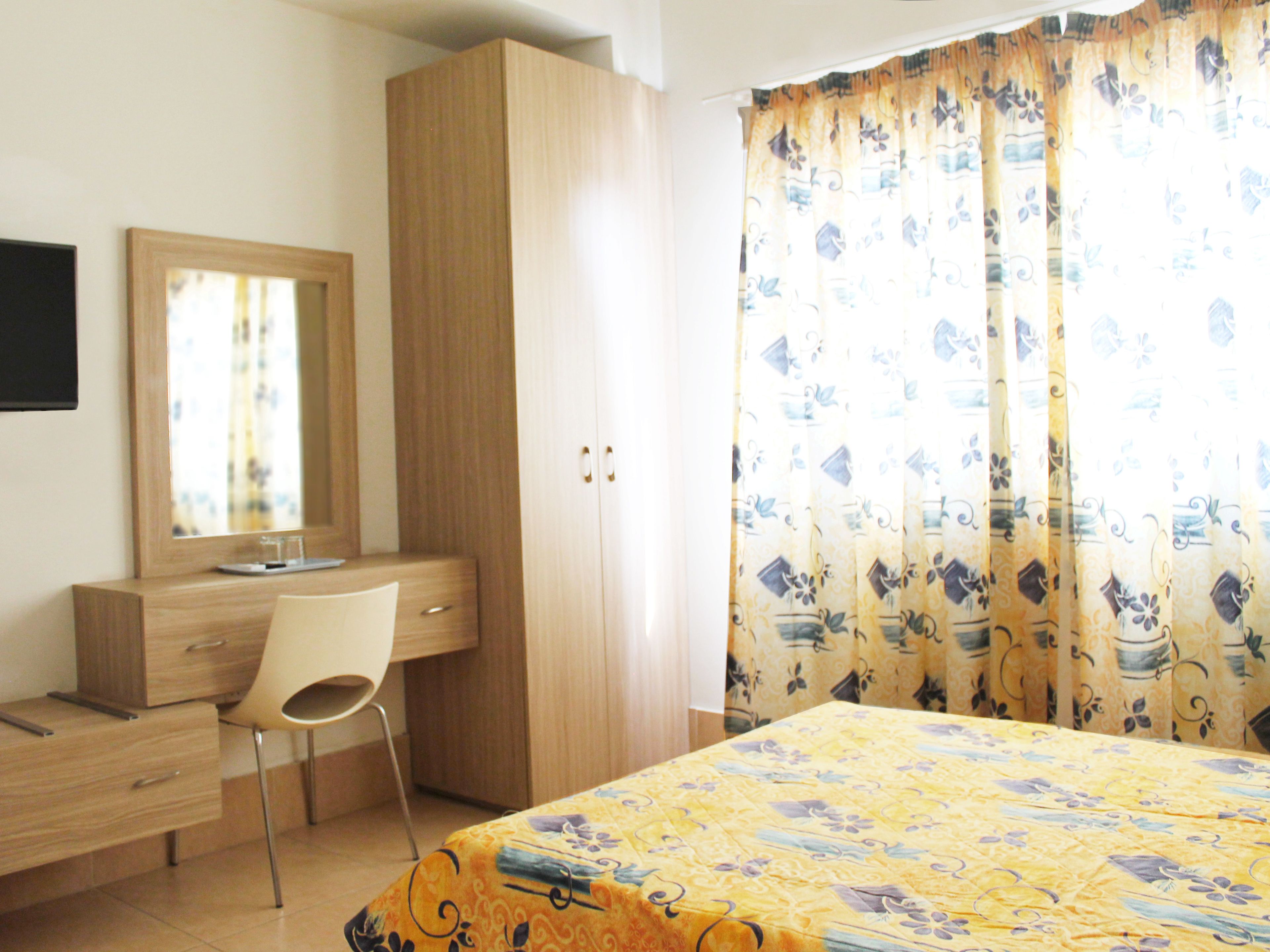 Ein Schlafzimmer mit Bett, Schreibtisch, Stuhl, Kleiderschrank und Spiegel.