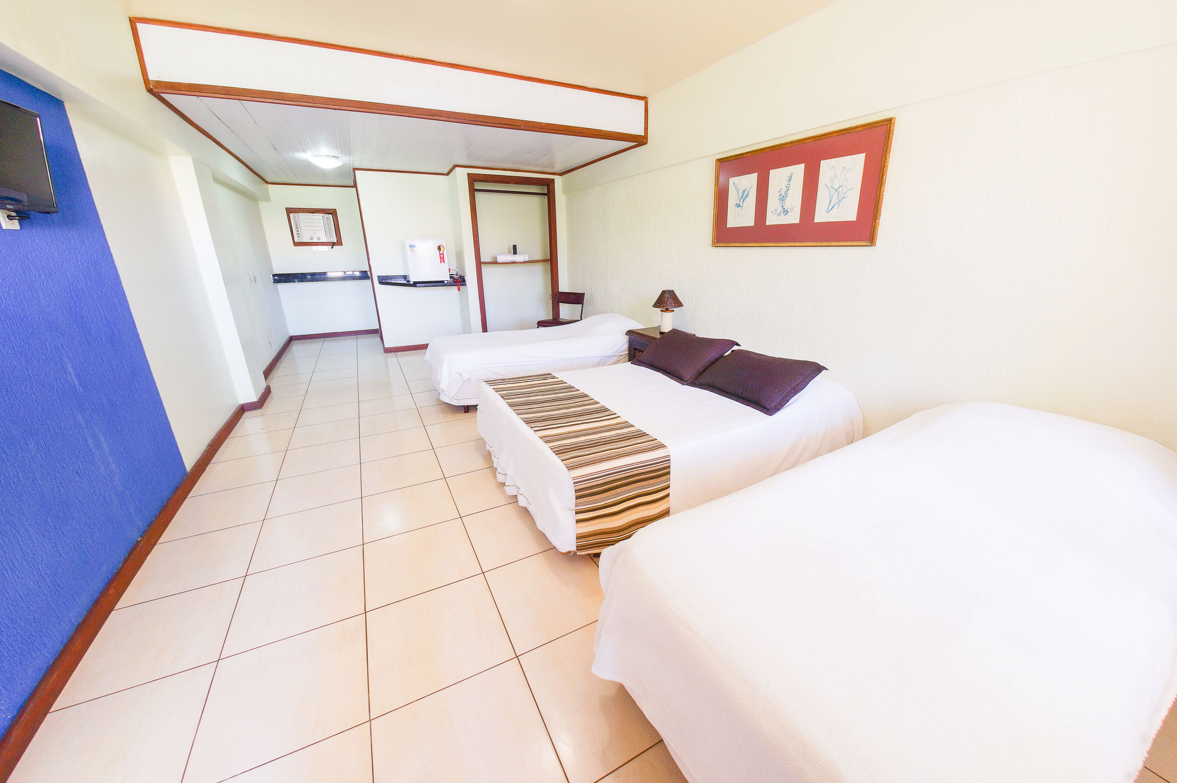 A hotel room with two beds, a desk, a chair, a TV, and a framed picture on the wall.