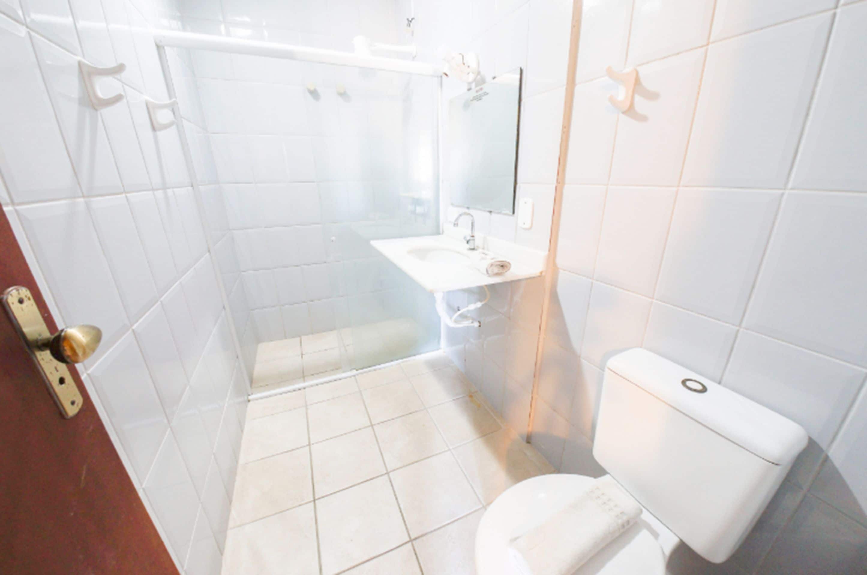 A bathroom with white tiles, a toilet, a sink, and a shower.