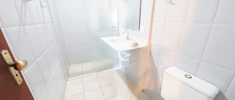 A bathroom with white tiles, a toilet, a sink, and a shower.