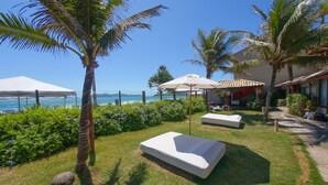 Un patio frente a la playa con un toldo blanco, una silla de descanso y una mesita.
