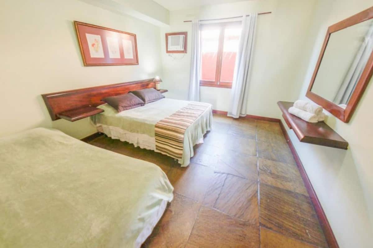 Una habitación con dos camas, cabecera de madera, una ventana con cortinas y un espejo en la pared.