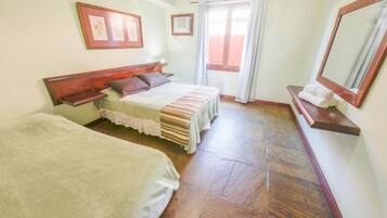 Una habitación con dos camas, cabecera de madera, una ventana con cortinas y un espejo en la pared.