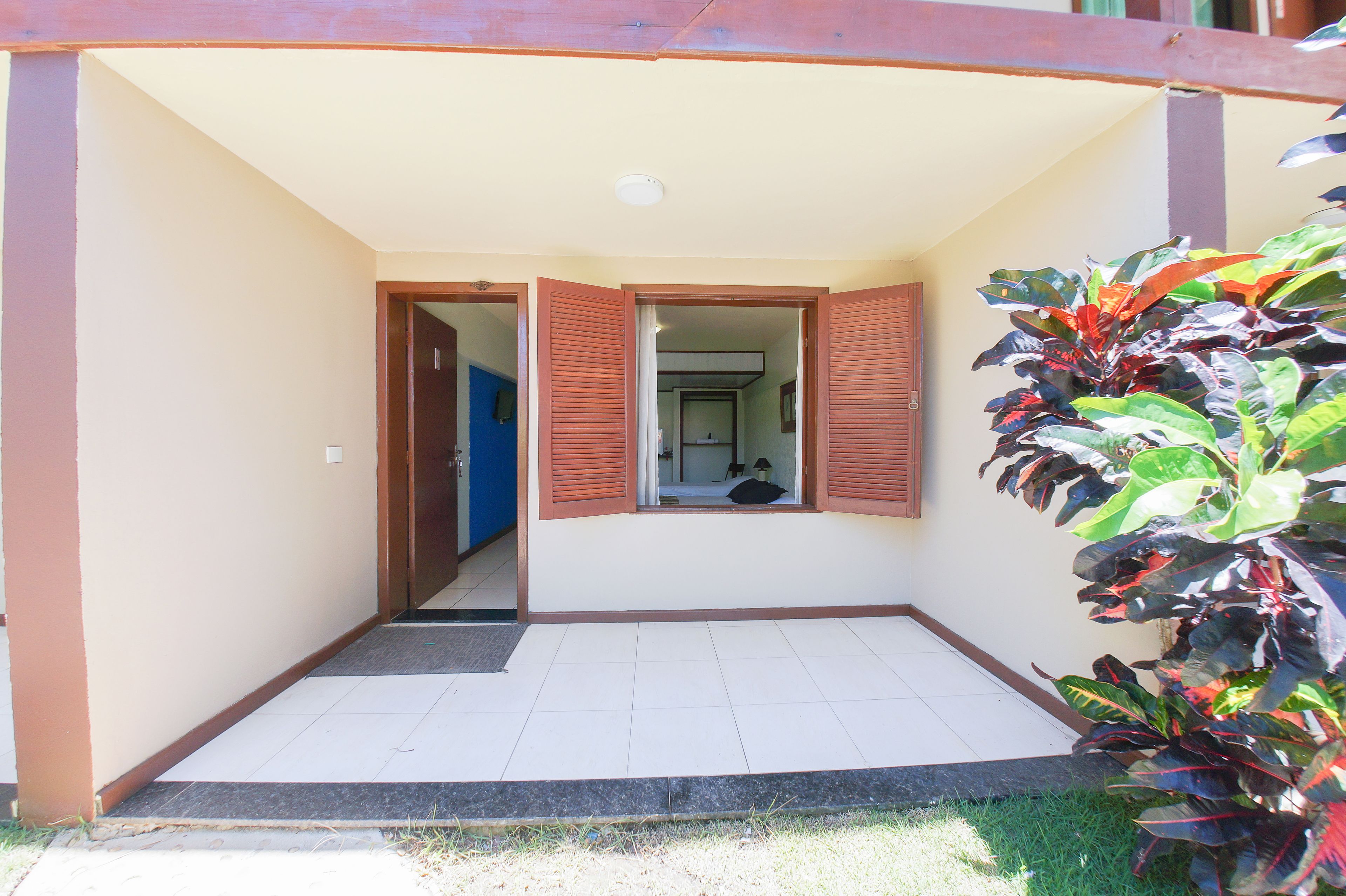 A covered entrance with a tiled floor, a blue door, and a window with brown shutters.