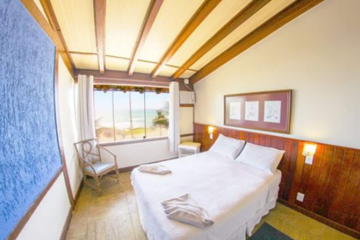 Una habitación de hotel con una cama, una silla, un ventanal con vistas y un cuadro en la pared.