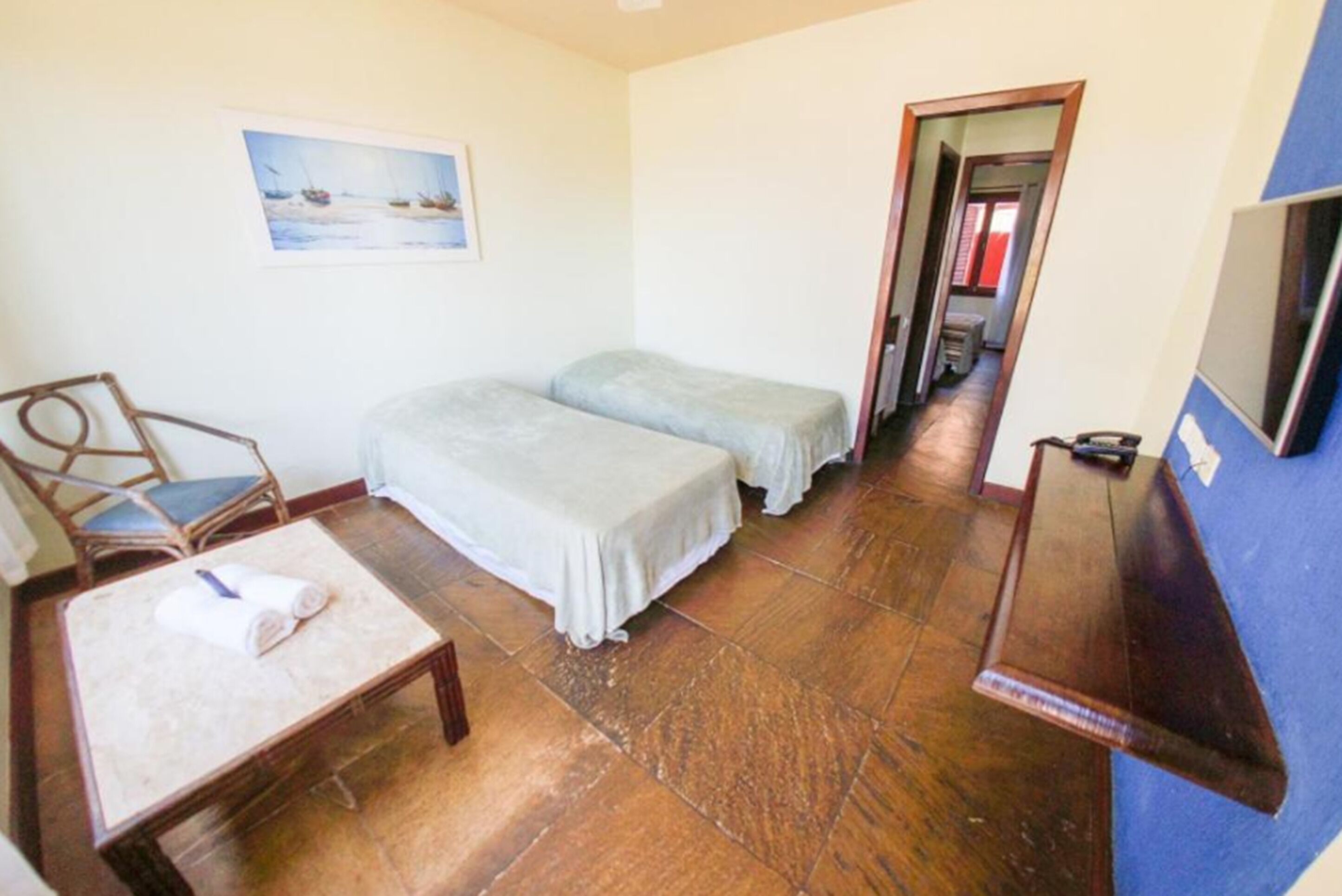 A small, clean room with two beds, a chair, a table, and a TV.