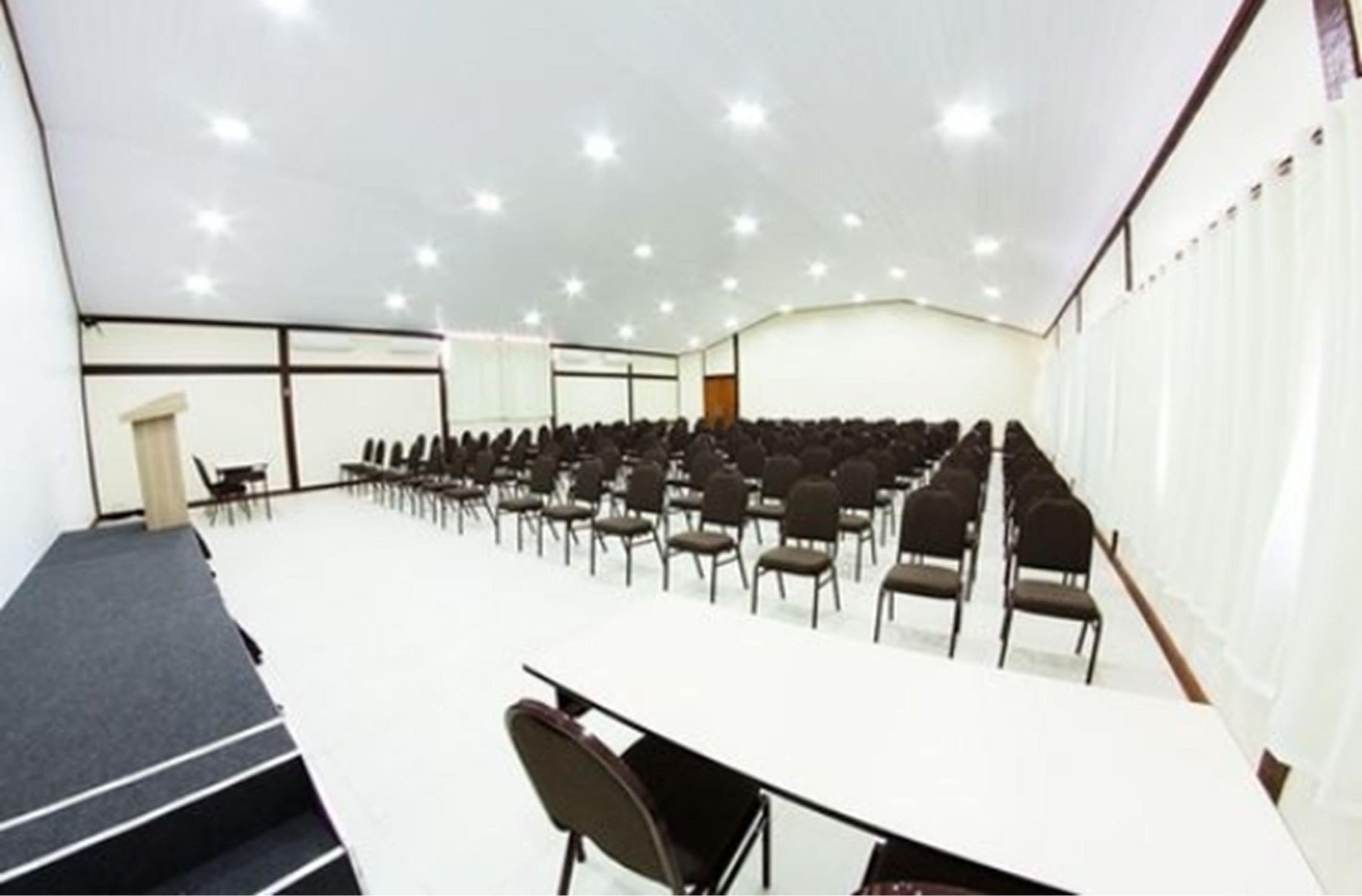 Una sala de conferencias con filas de sillas, una mesa larga y un escenario.