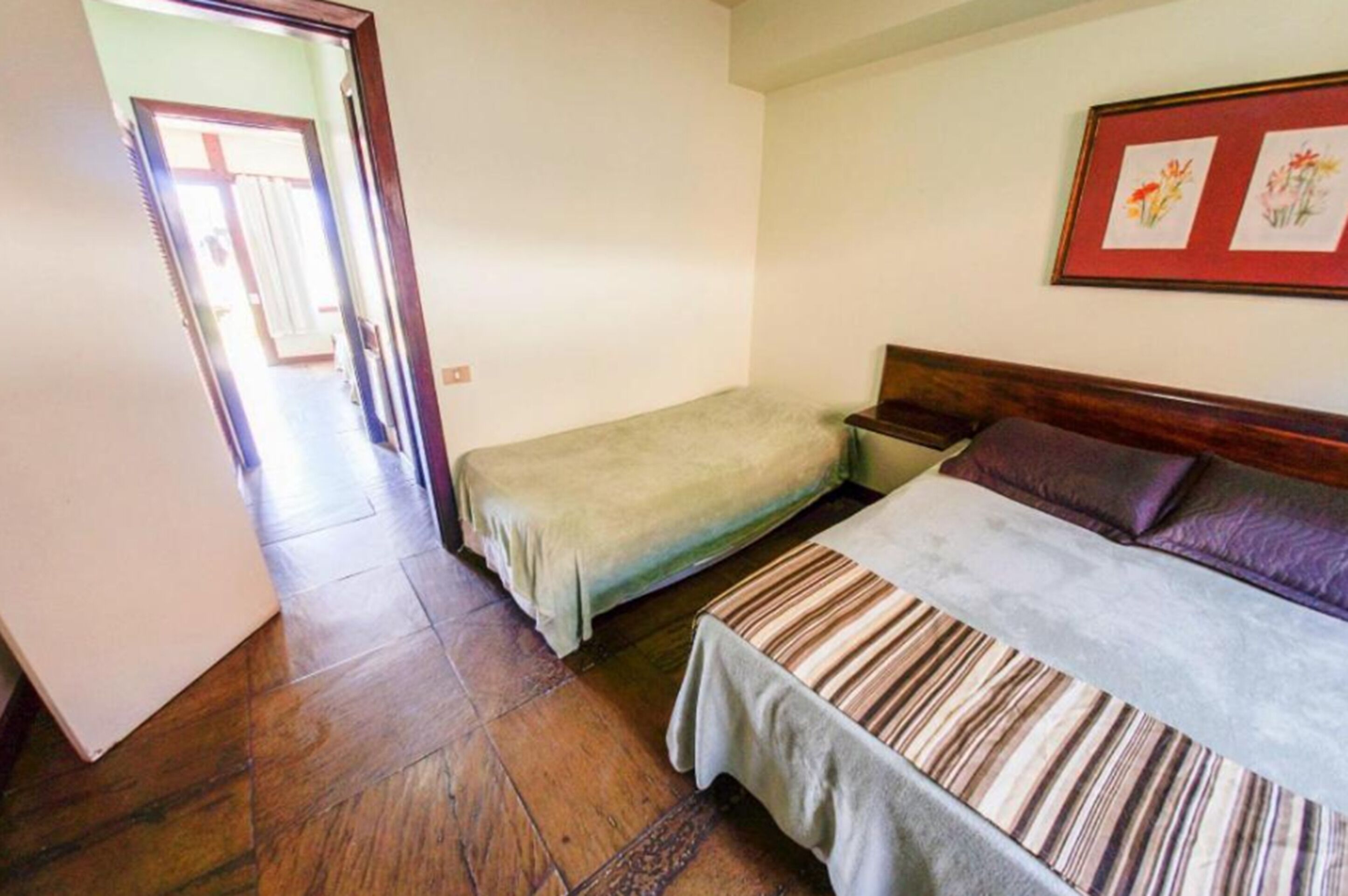 A bedroom with a large bed, a smaller bed, a nightstand, and a framed picture on the wall.