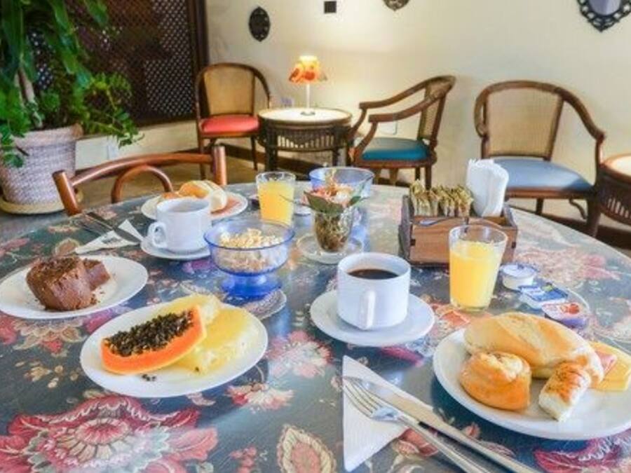 Mesa de jantar com itens de café da manhã, cadeiras e um vaso de planta.
