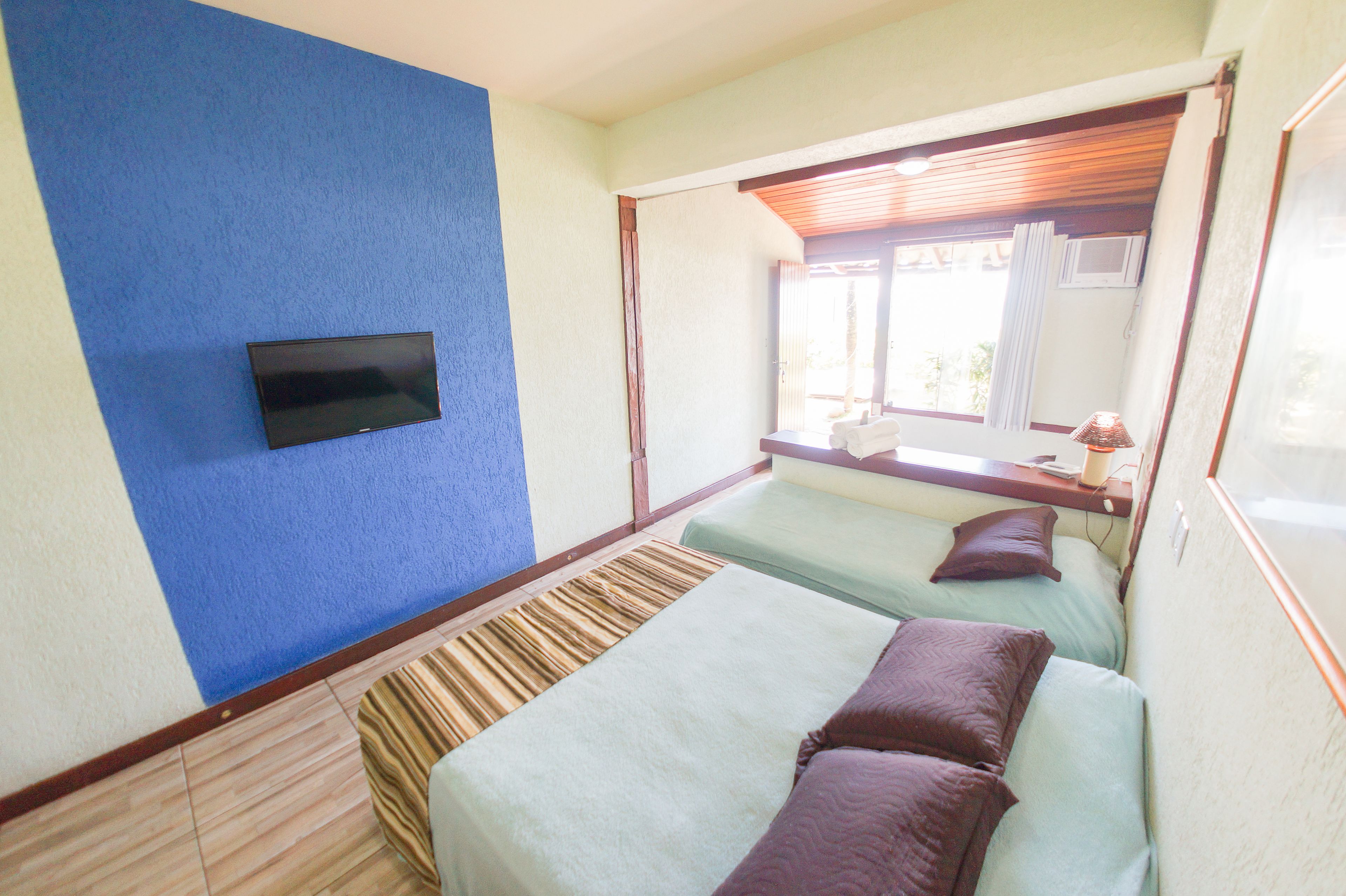 A hotel room with two beds, a flat-screen TV mounted on the wall, and a window with curtains.