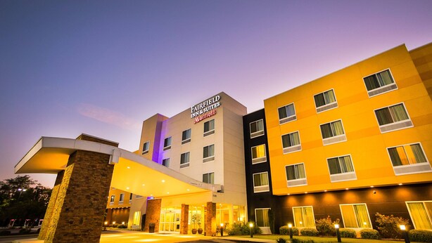 A Fairfield Inn & Suites Marriott hotel with a modern design, featuring a well-lit entrance and a landscaped outdoor area.