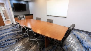 A conference room with a long wooden table, four chairs, a whiteboard, and a flat-screen TV on the wall.