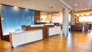 A hotel reception area with a wooden reception desk, a blue textured wall, and a seating area with a view of the city.