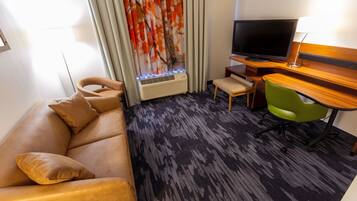 Habitación de hotel con sofá de cuero, una mesita, una silla verde, un televisor de pantalla plana y una ventana con cortinas.