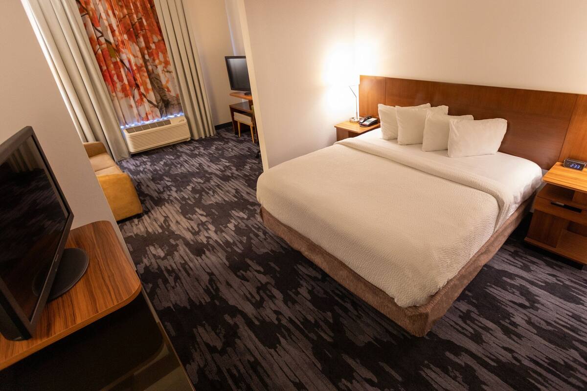A hotel room with a large bed, a desk with a computer, a TV, and a window with curtains.