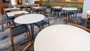 A restaurant with round tables and chairs, booths, and a TV screen.