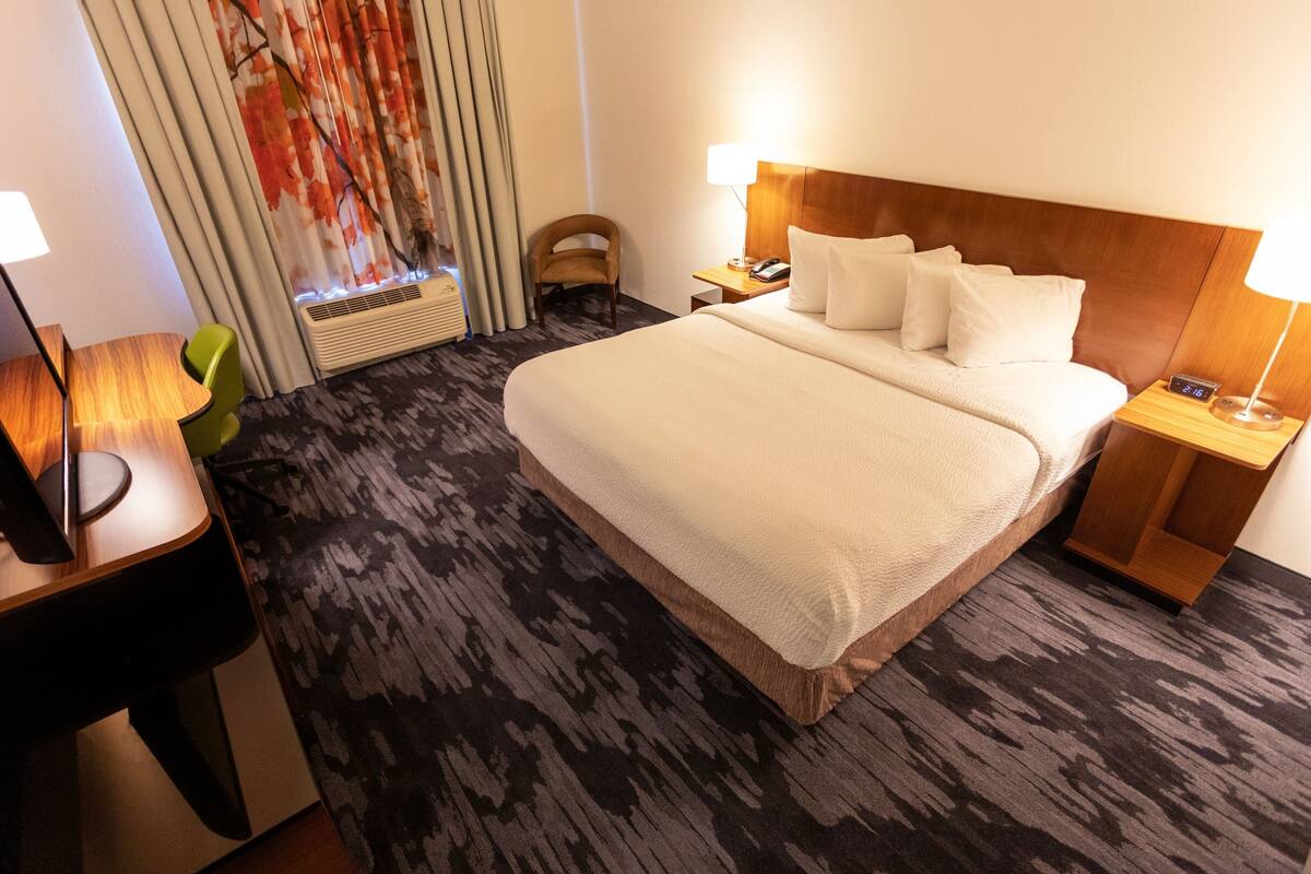 A hotel room with a large bed, two bedside tables with lamps, a chair, and a window with curtains.