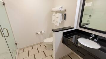Un baño moderno con cabina de ducha de vidrio, inodoro blanco, lavamanos negro con espejo y toallero con toallas dobladas.