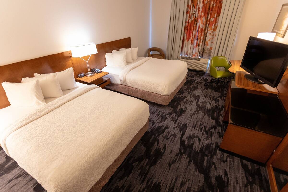 A hotel room with two beds, a TV, a desk, and a chair.