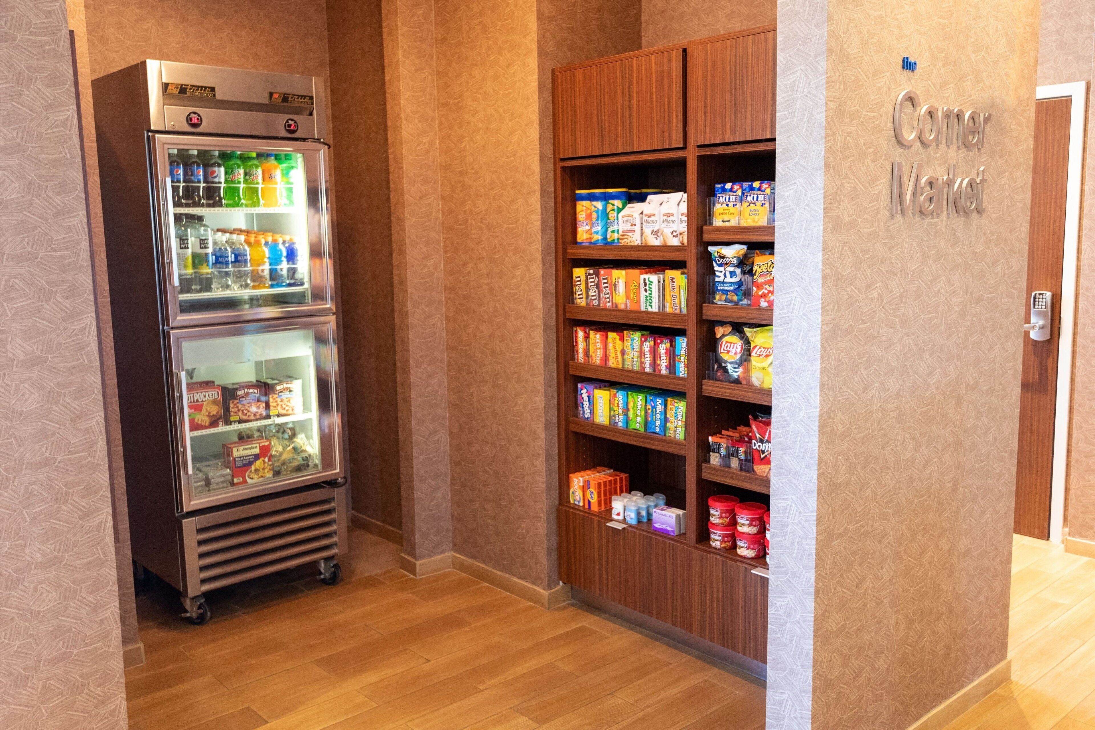Máquina expendedora con snacks y bebidas, un letrero de Corner Market y un mueble de madera con snacks.