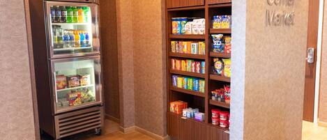 Máquina expendedora con snacks y bebidas, un letrero de Corner Market y un mueble de madera con snacks.