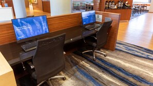 A hotel reception area with two computer workstations, a reception desk, and a seating area with tables and chairs.