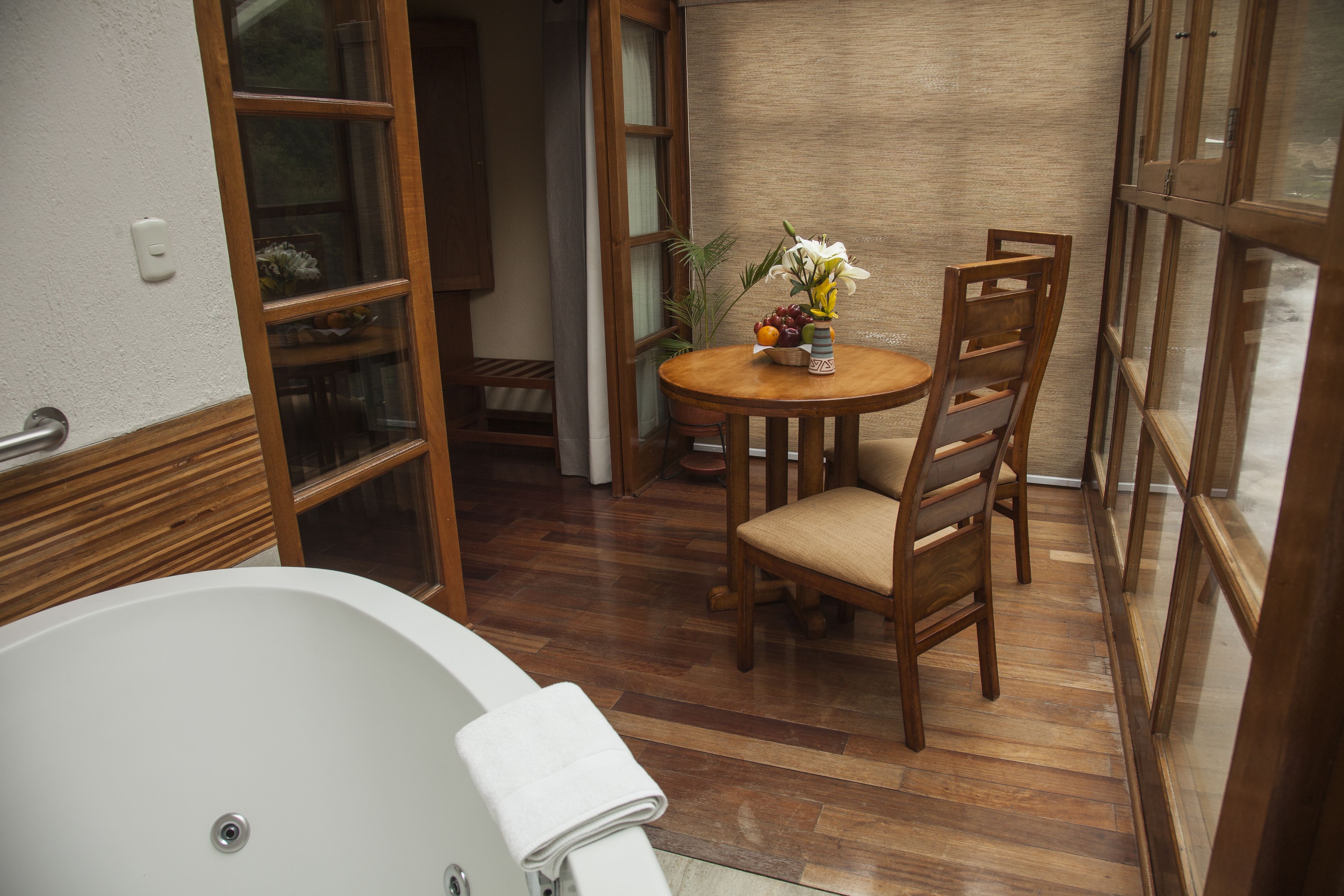 Un baño con bañera, suelo de madera, una mesa redonda con sillas y un florero con flores.