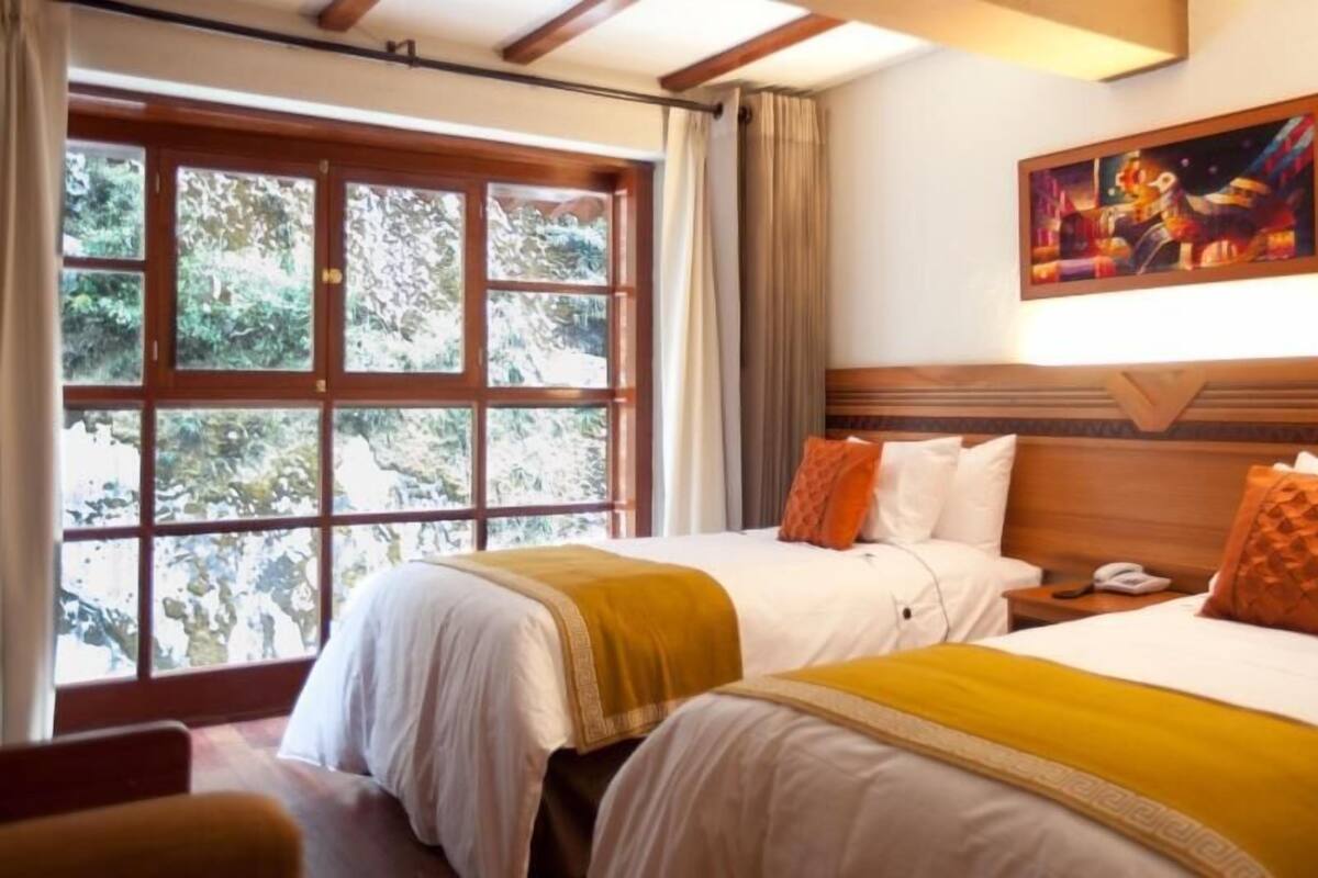 A hotel room with two beds, a large window with a view of trees, a painting on the wall, and a wooden headboard.