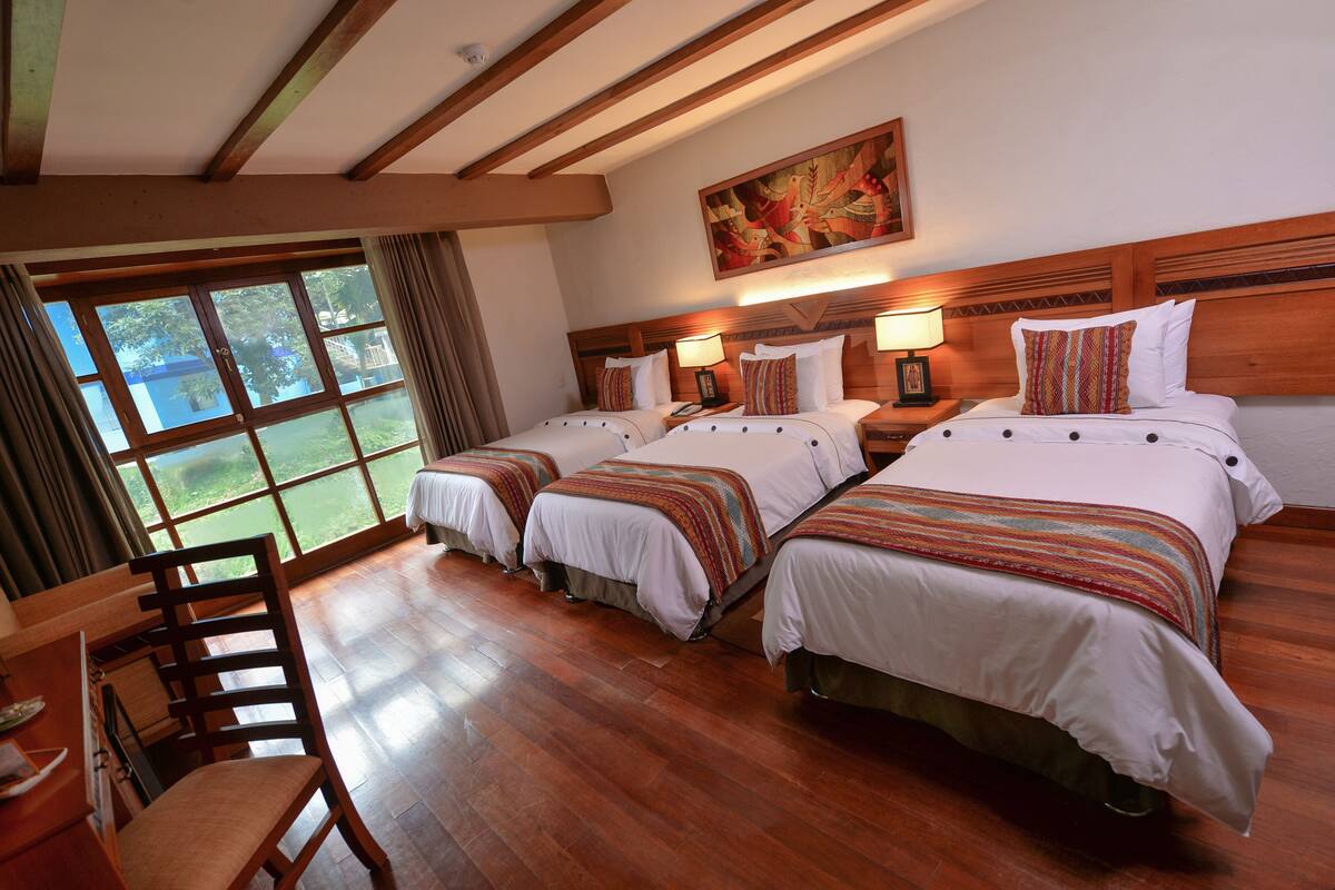A hotel room with two beds, wooden flooring, a desk, and a chair.