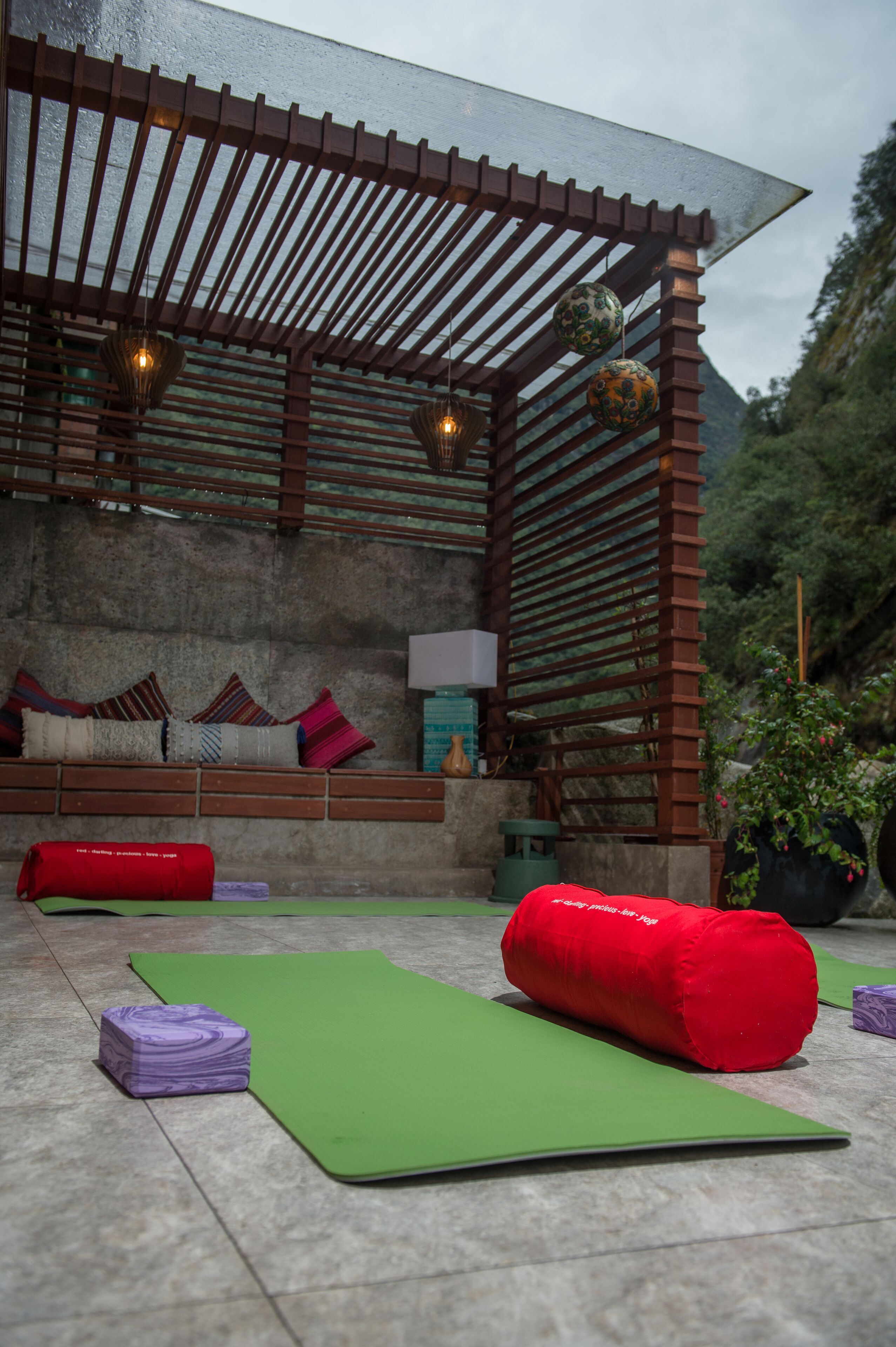 Un espacio al aire libre para yoga con colchonetas, cojines y una estructura de pérgola de madera.