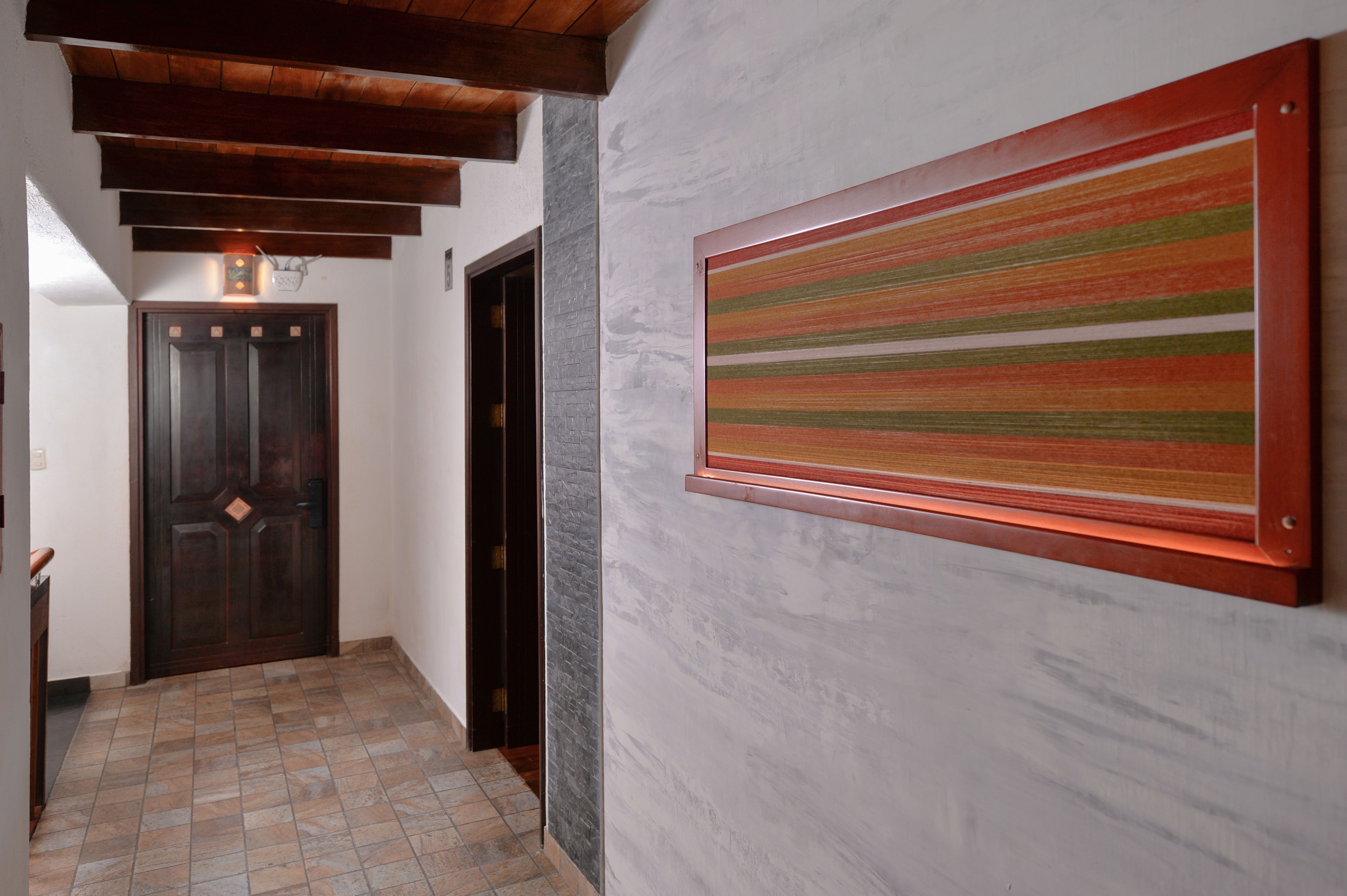 A hallway with a wooden door, a stone wall, and a colorful striped artwork.