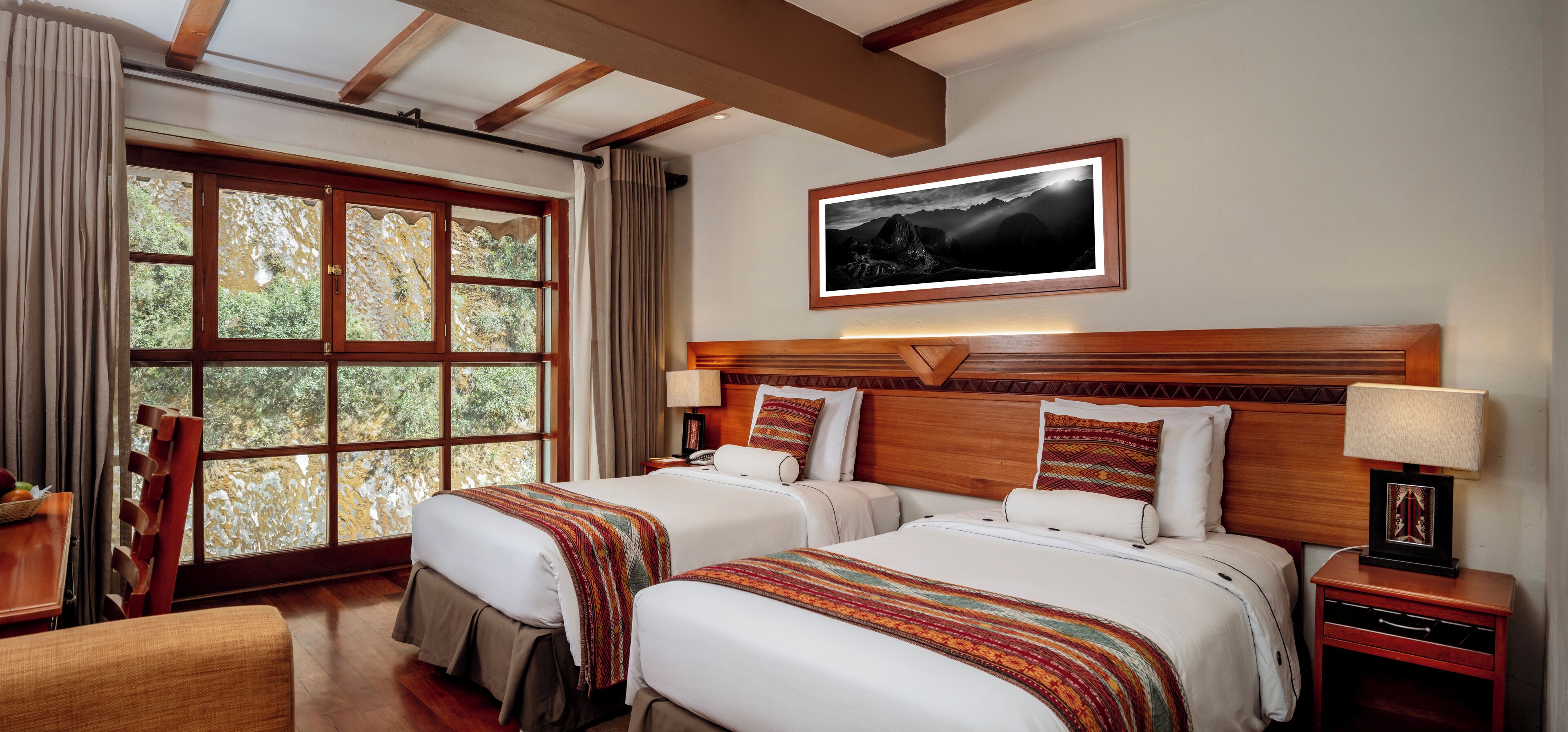 A hotel room with two beds, a large window with a view of trees, a wooden headboard, and a framed picture on the wall.