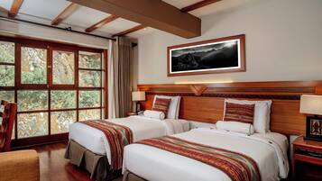 A hotel room with two beds, a large window with a view of trees, a wooden headboard, and a framed picture on the wall.