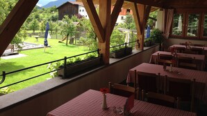 A restaurant with outdoor seating, wooden beams, and a view of a garden and mountains.
