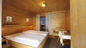 A wooden cabin room with a large bed, a small table, and a chair.