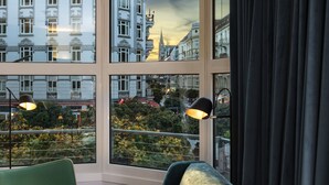 A room with a large window offering a city view, a green chair, a black sofa, and two table lamps.