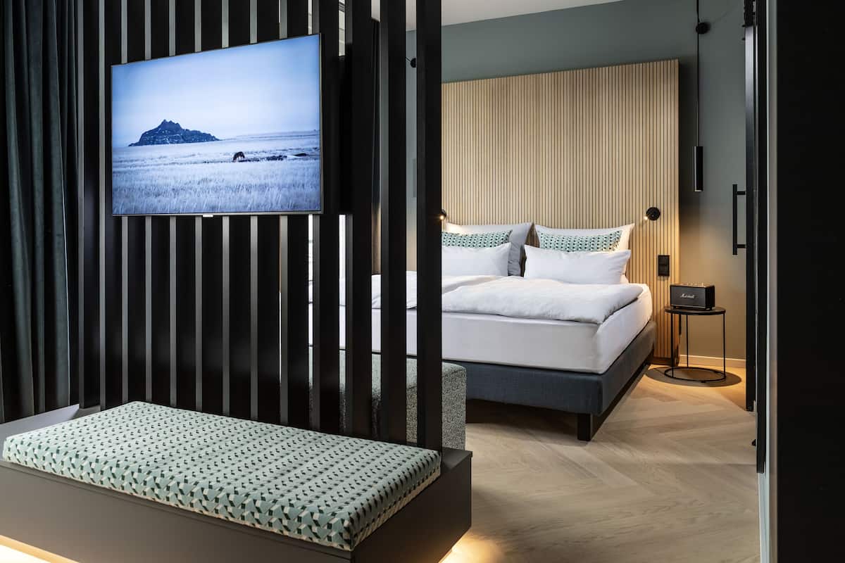 Una habitación de hotel moderna con una cama, una zona de estar, un televisor y una mesita.